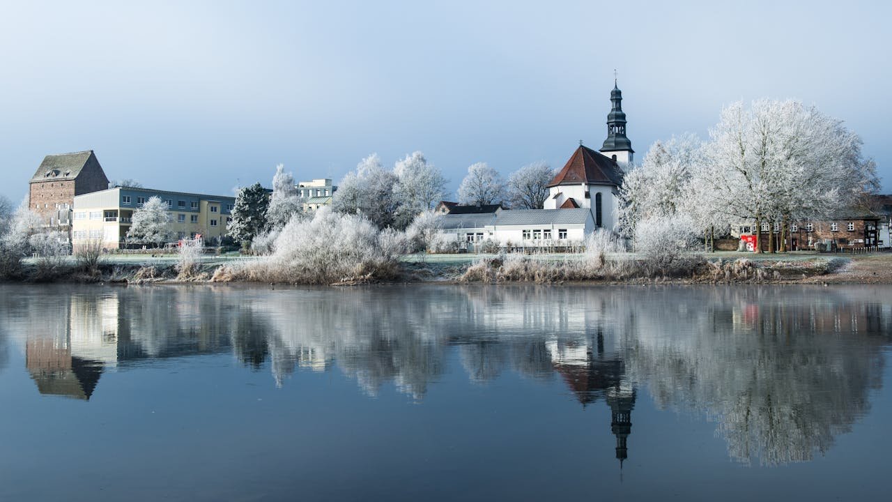 Peaceful winter view of Beverungen, Germany with a church and lake reflection.